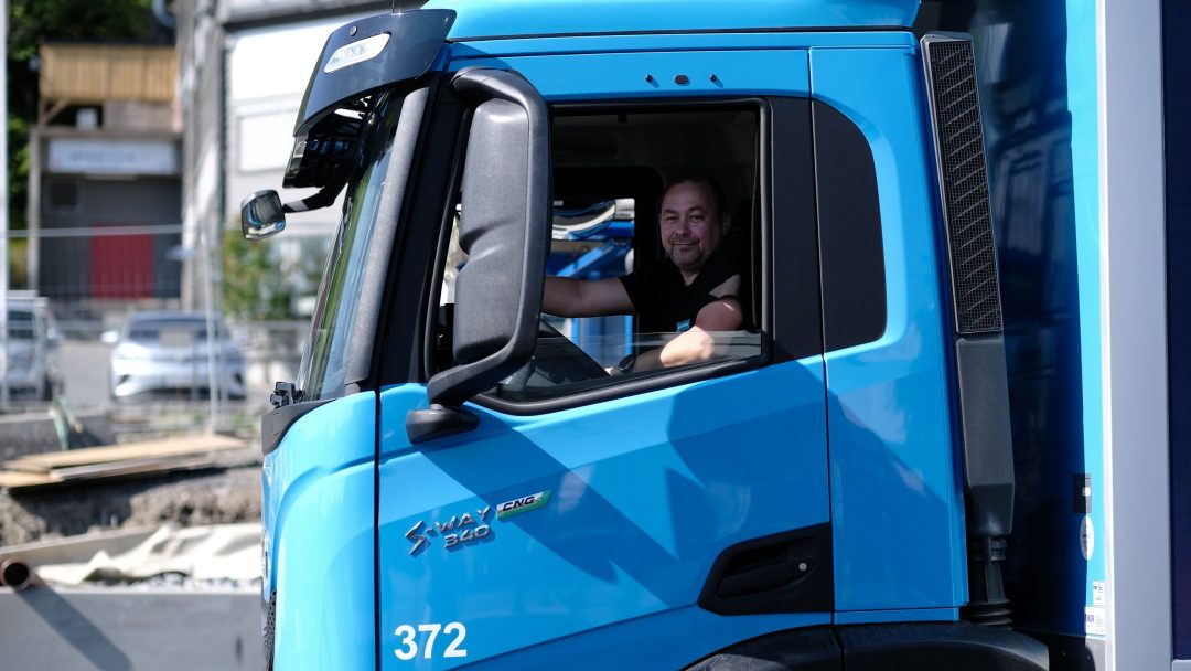 En mann som sitter i førersetet på en blå lastebil på en energistasjon.