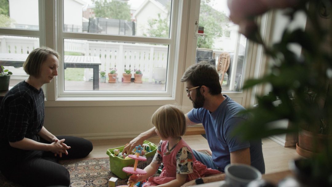 Familie på tre sitter på gulvet i stua og leker