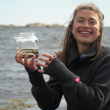 jente viser frem glasskrukke med funn fra havet