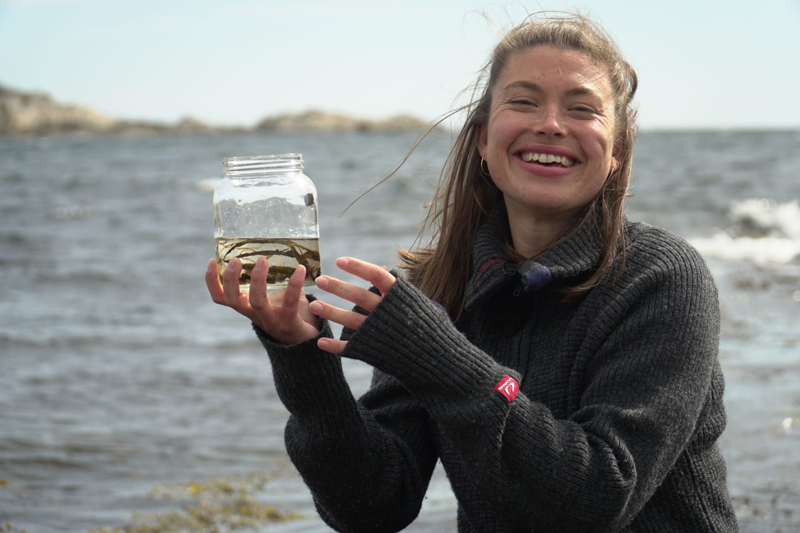 En kvinne som holder en krukke med tang under et klimaforedrag ved havet.