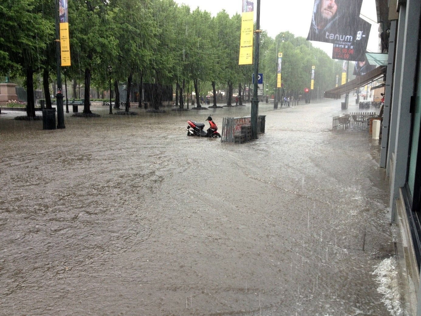 En scooter som står parkert med hjulene i overvann etter styrtregn i Karl Johans gate.