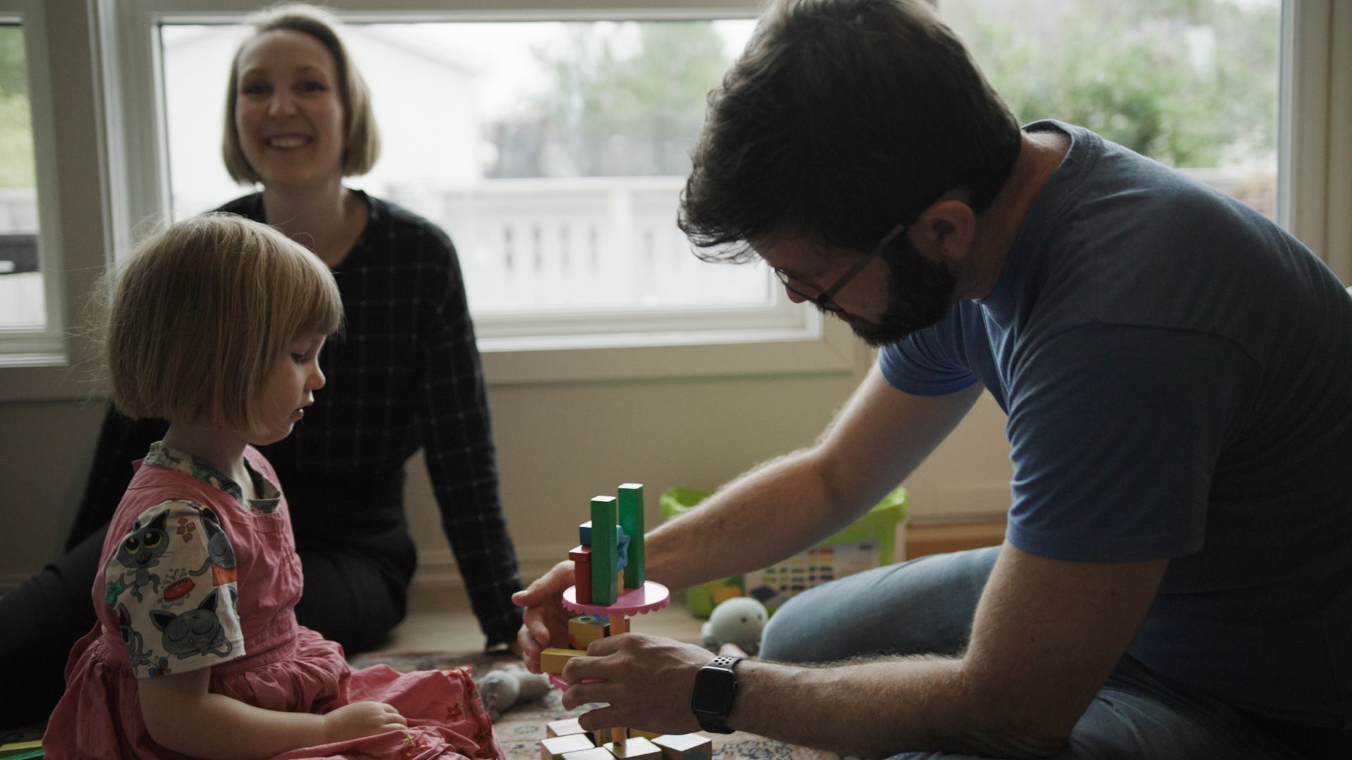 En mamma og pappa sitter på gulvet i stua og leker med barnet sitt.