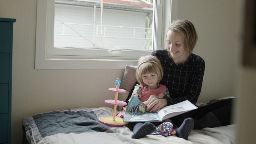 mor og datter sitter på gulvet og leser i en bok foran et vindu