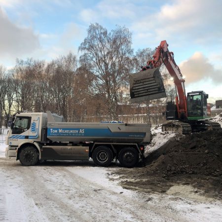 elektrisk gravemaskin fyller jord på lasteplanet i elektrisk lastebil