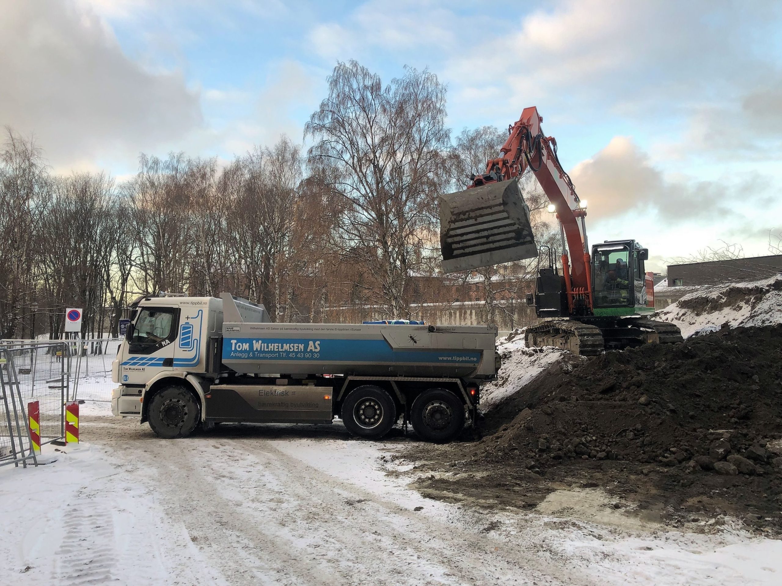 electric excavator shovels earth into the cargo bed of an electric truck