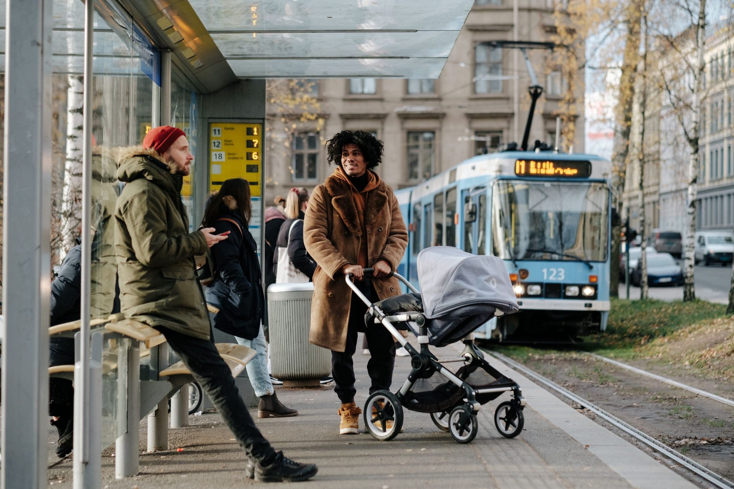 bilde av mann og dame med barnevogn på en bussholdeplass