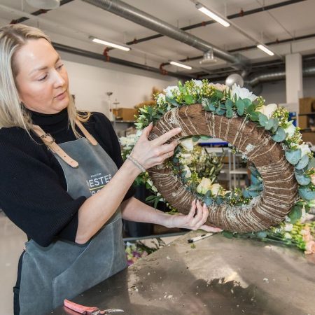 Blomsterdekoratør holder en blomsterkrans til grav. Setter den sammen.