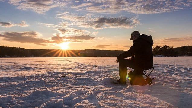 Mann som isfisker på innsjø i solnedgang