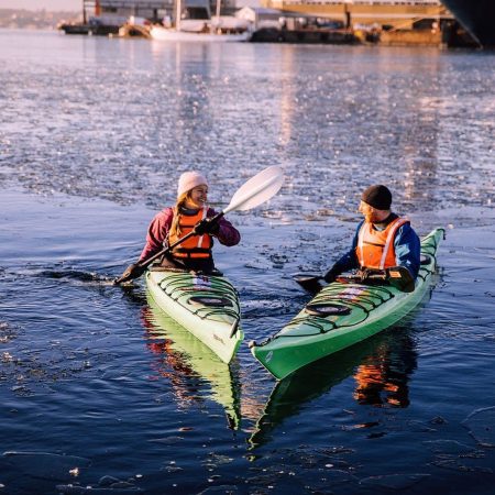 Kvinne og mann gjør vinteraktiviteter i hver sin grønne kajakk på sjøen