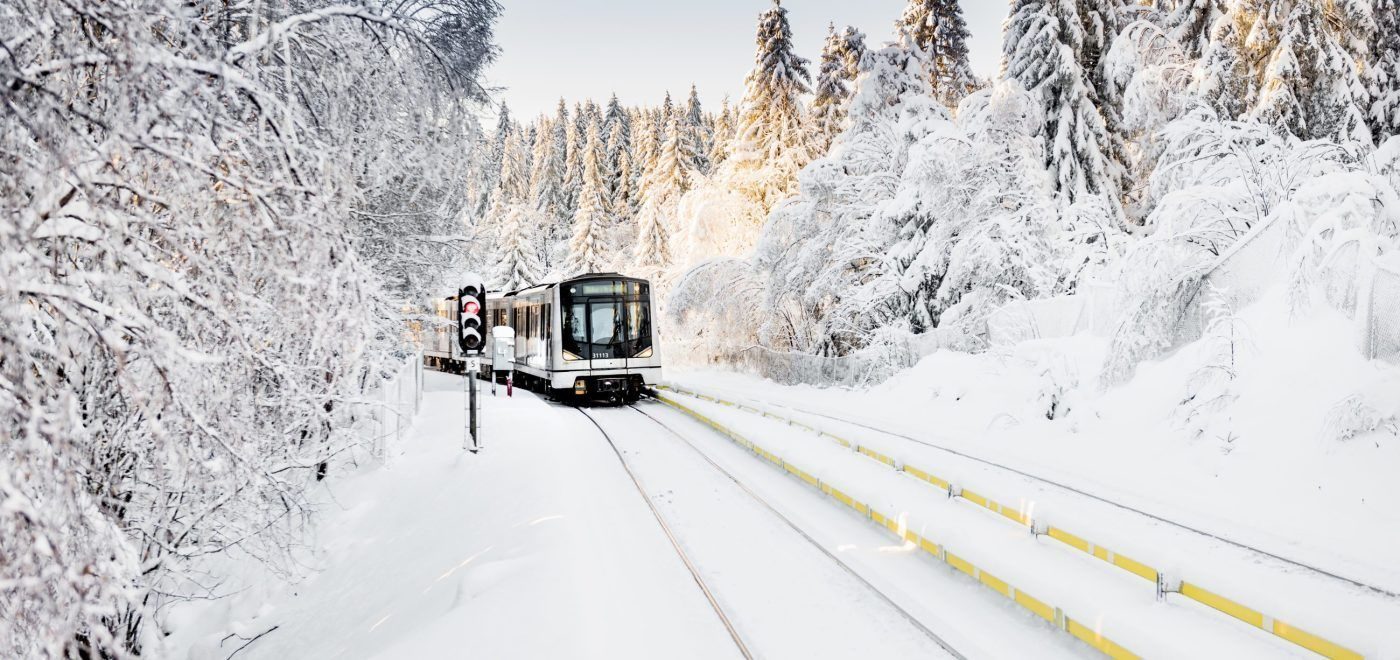 T-bane som kjører i vinterlandskap, omgitt av snøtunge trær