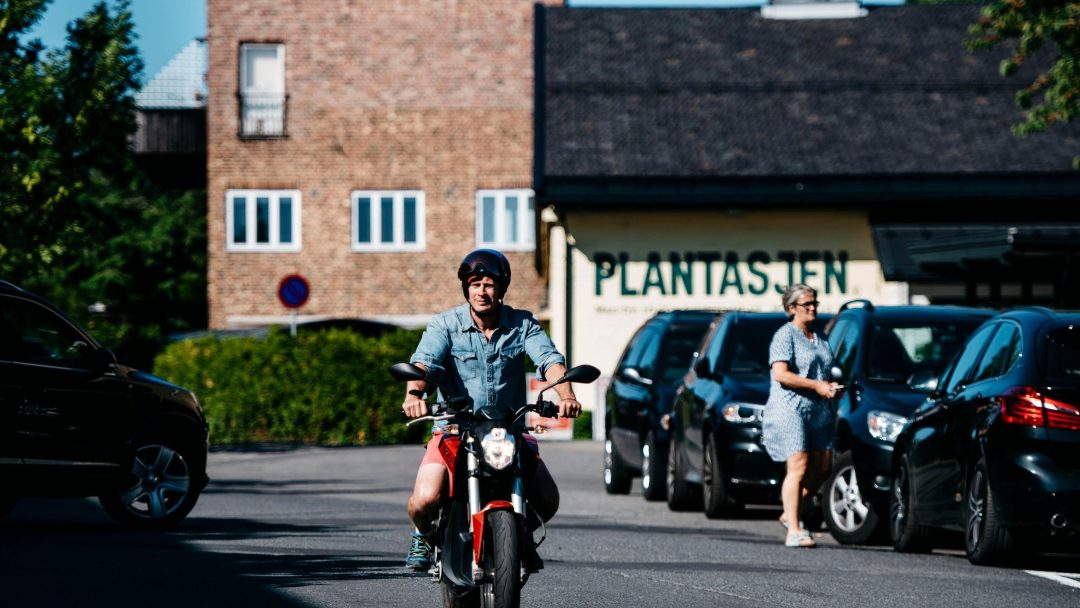 En mann som kjører en elmotorsykkel nedover en gate.