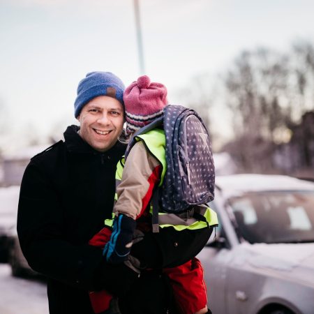 mann som bærer et barn med ryggesekk på fortau