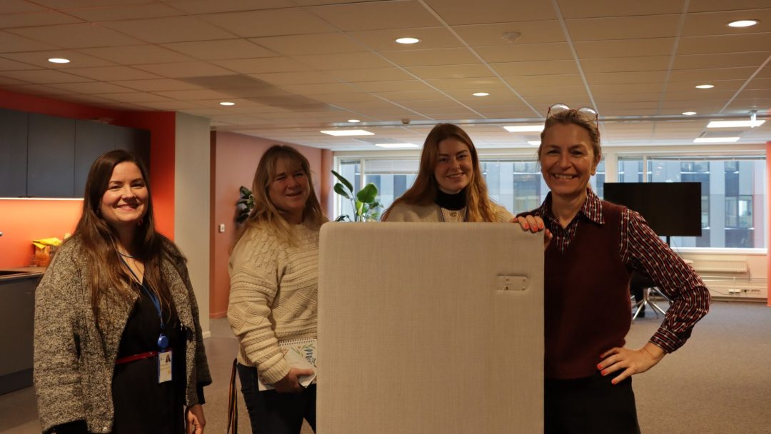 Fire kvinner står ved siden av en hvit boks på et kontormøblerkontor.