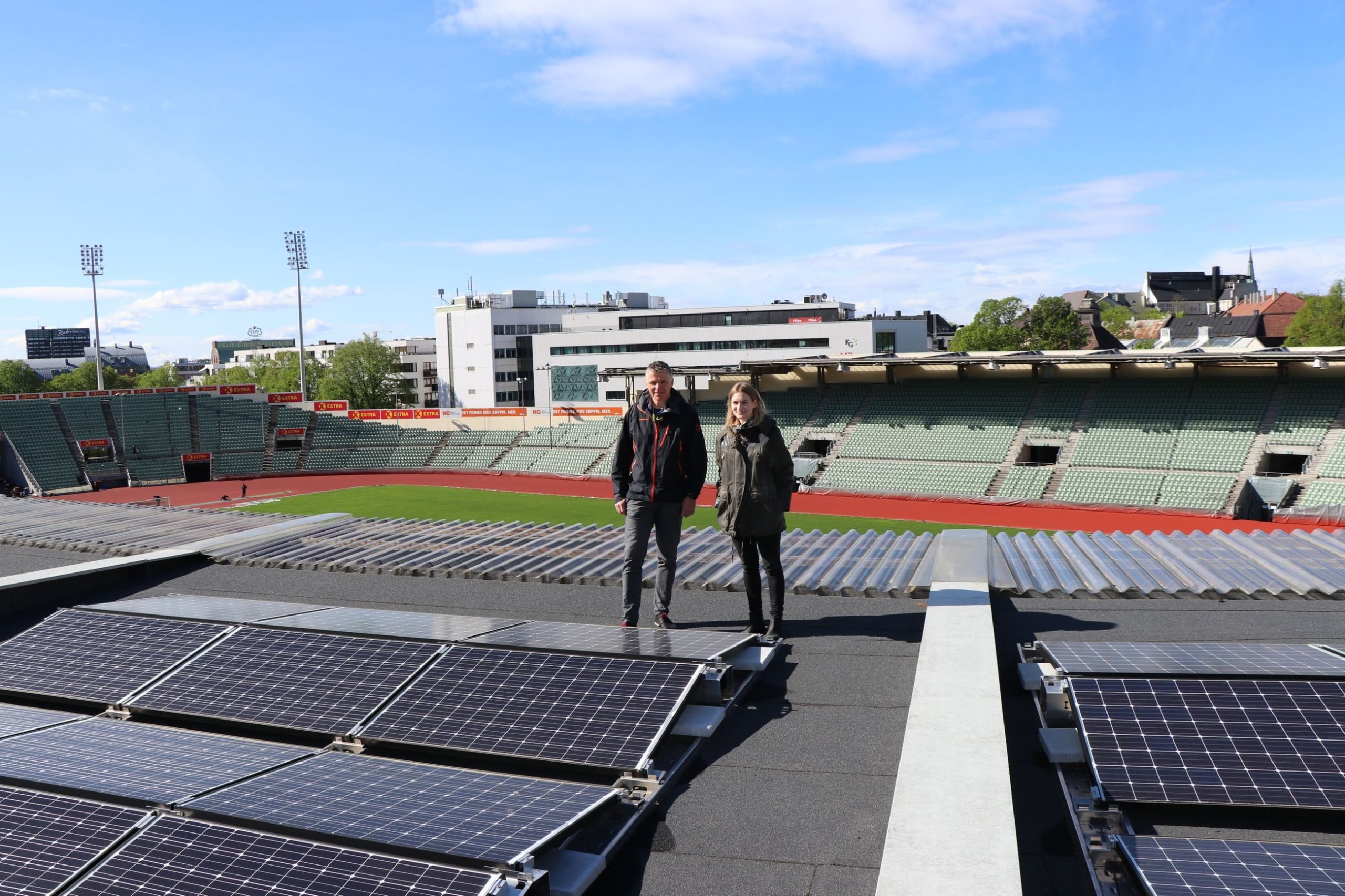 to personer skuer utover solcelleanlegget som bader i sol på et tak