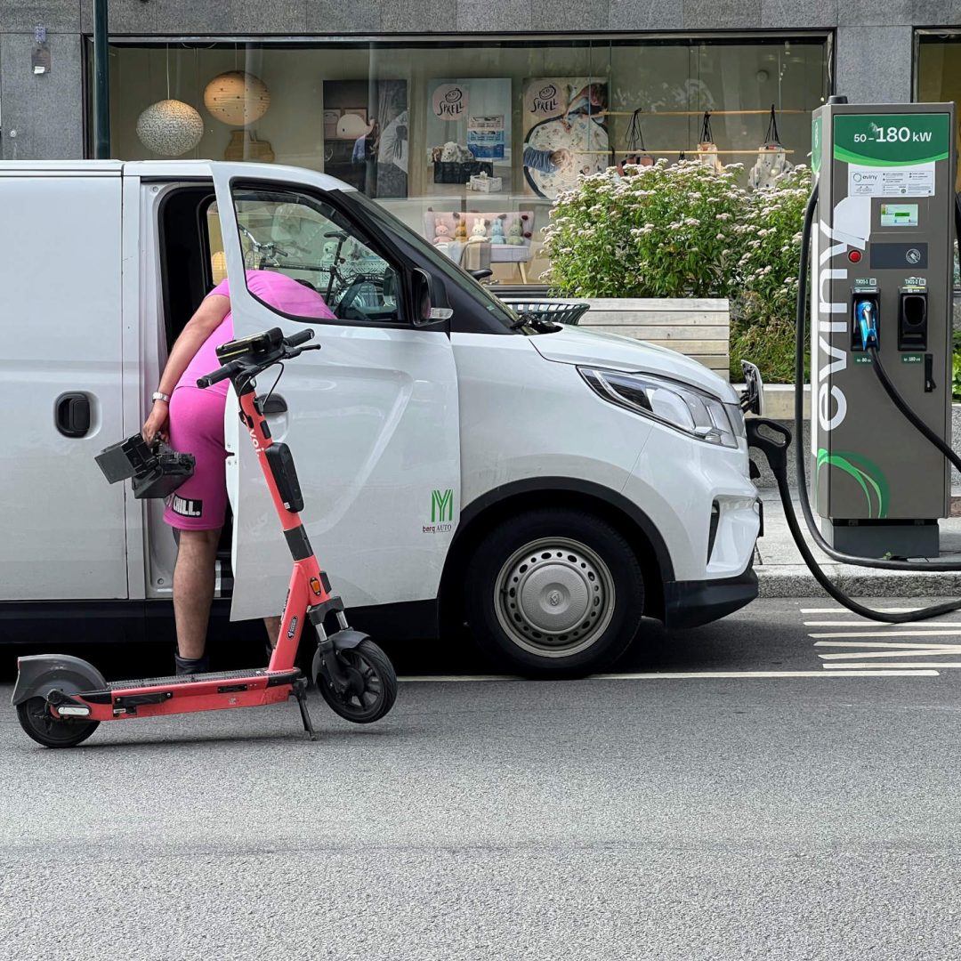 En elektrisk sparkesykkel står parkert ved siden av en hvit varebil.