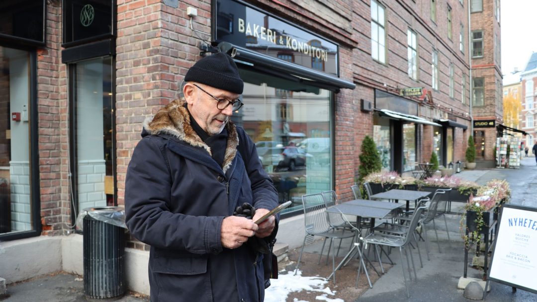 Svein Gulbrandsen står på gata og ser på mobilen sin.