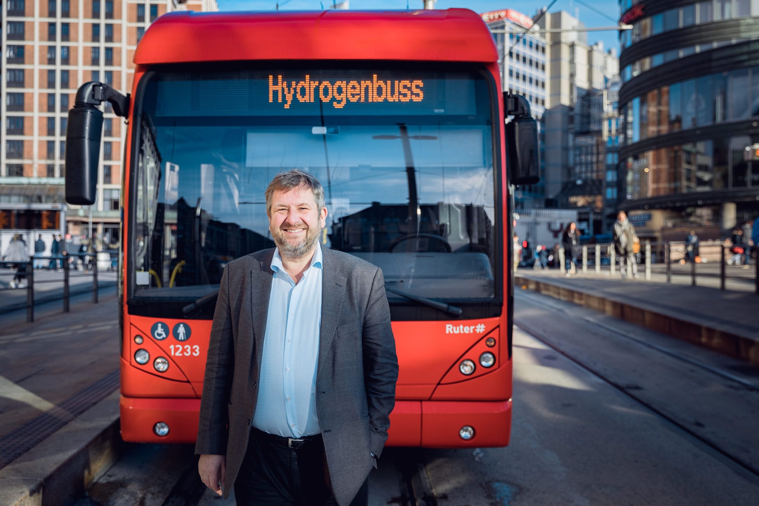 Bernt Reitan Jenssen i Ruter står foran en av de røde hydrogenbussene i Oslo sentrum.
