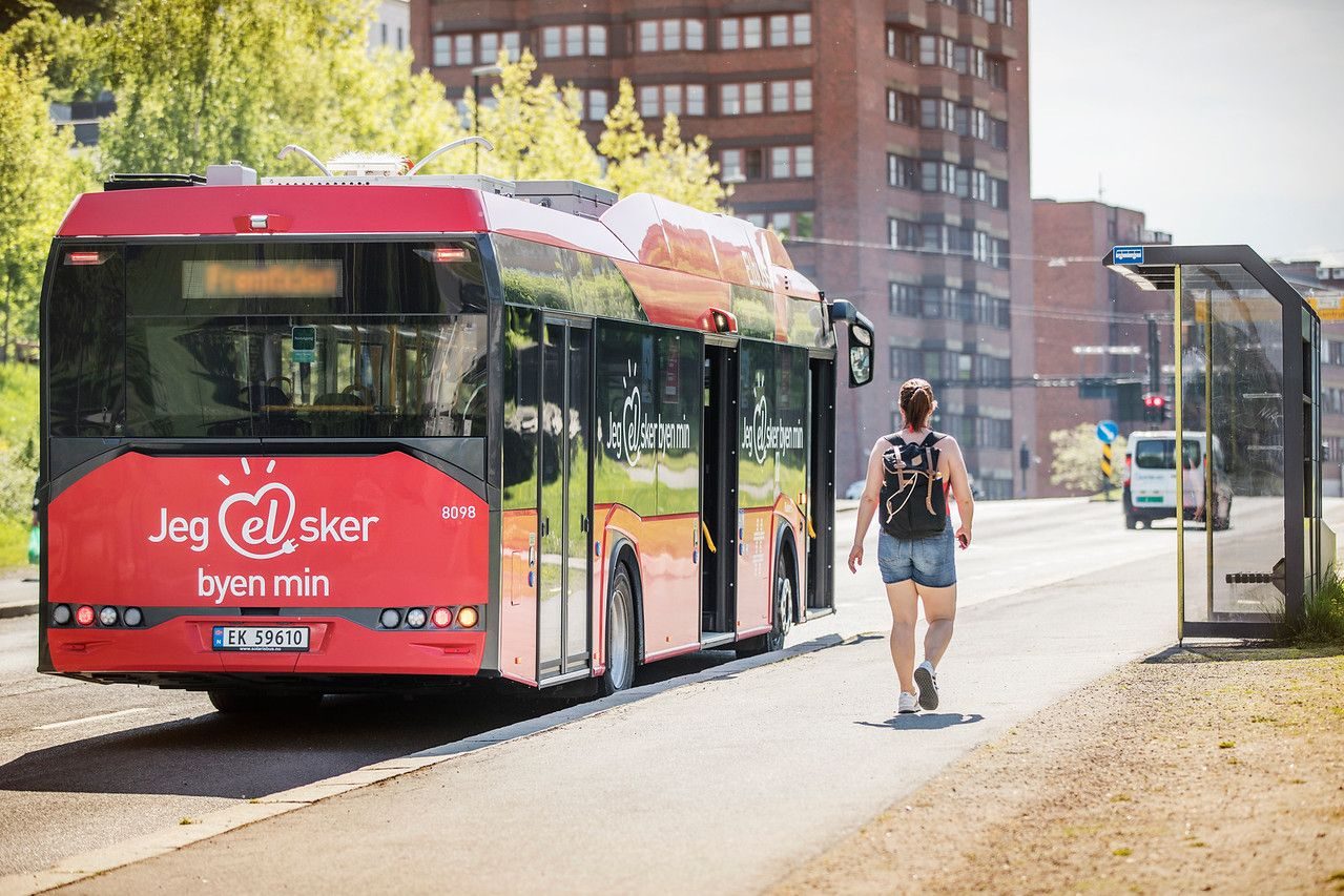 dame på fortau ved siden av en elbuss