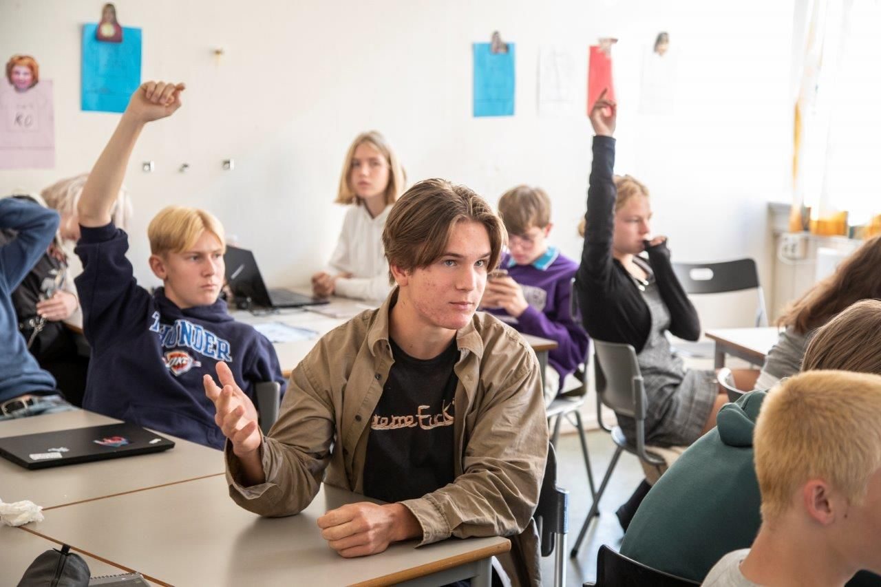 En gruppe elever i et klasserom rekker opp hendene under et klimaforedrag.