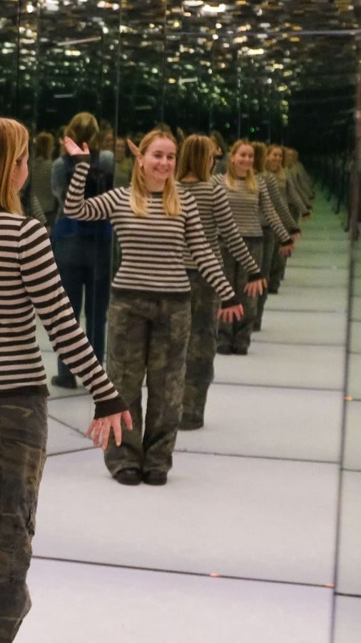 Kvinne i stripete genser i rom med speil som gir illusjon av uendelig med speilbilder
