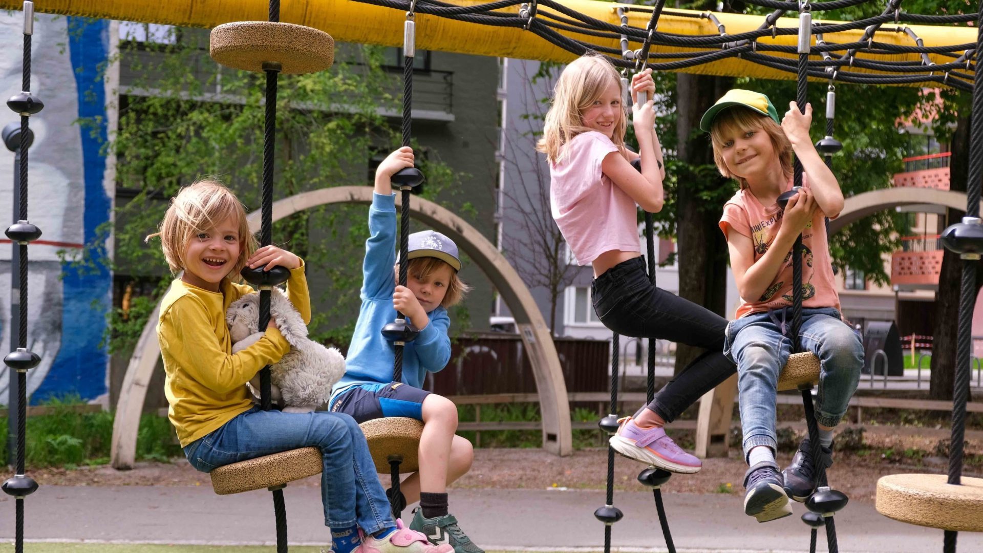 De fire barna henger i en lekestativhuske hver og smiler til kameraet.