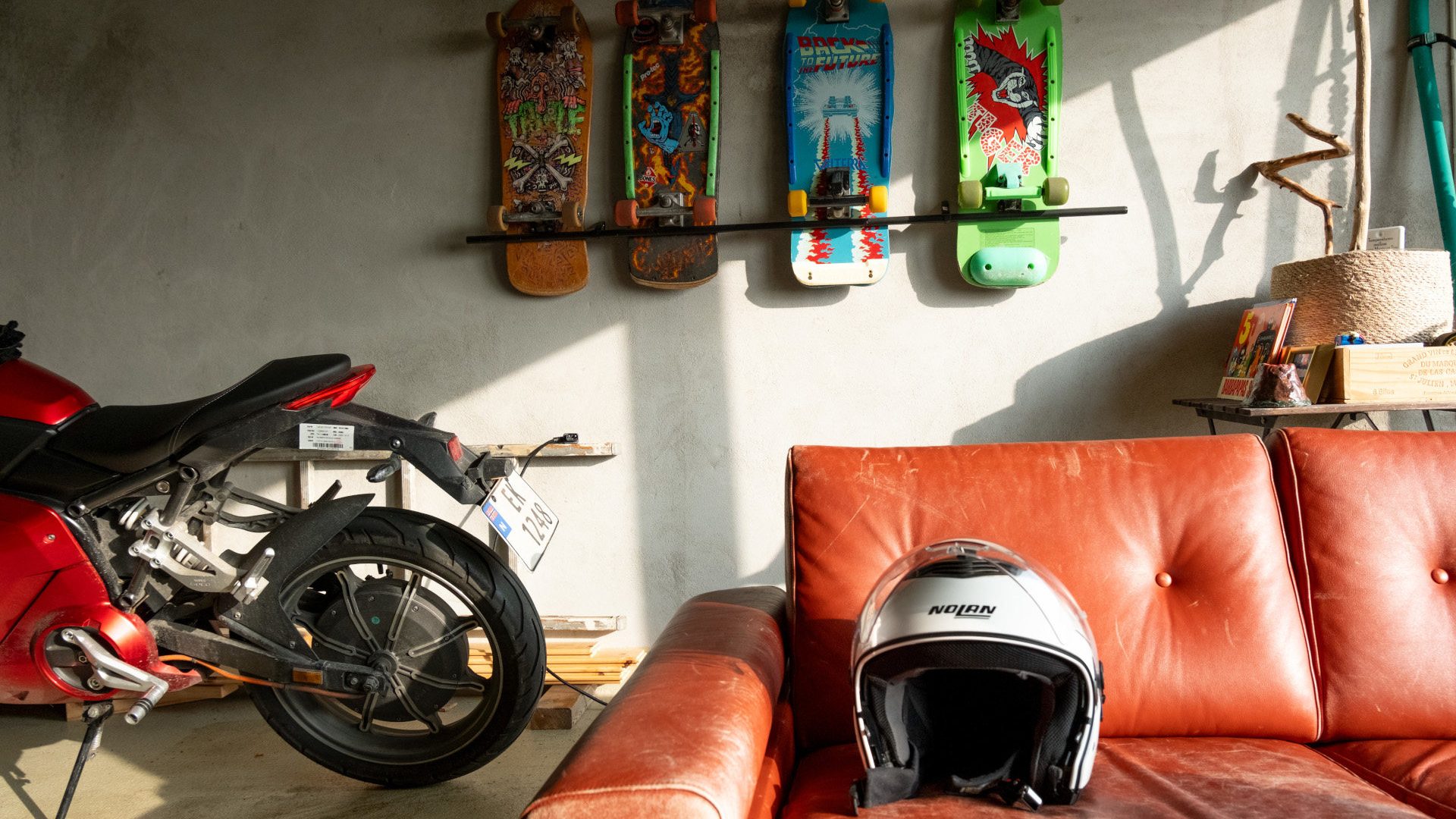 Bilde av en motorsykkelhjelm på en sofa, med skateboard hengende på en vegg bak.