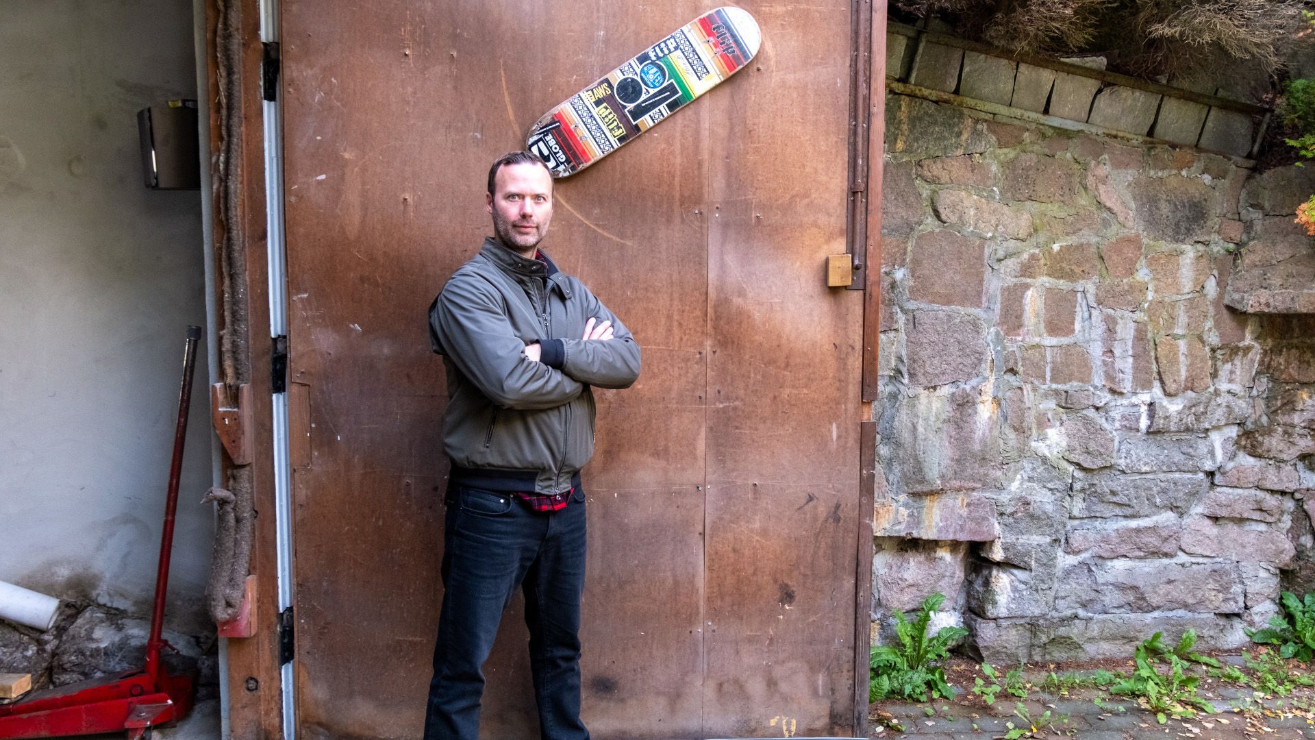 Tim står foran en garasjedør med et skateboard.