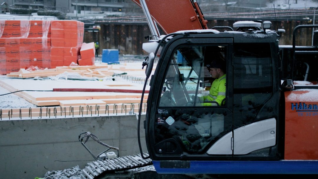 En bygningsarbeider sitter i en utslippsfri gravemaskin på byggeplassen.