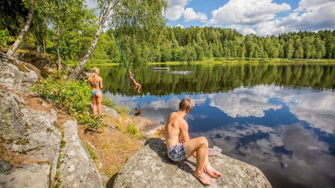 Tre personer som bader. Den ene slenger seg uti med et tau.