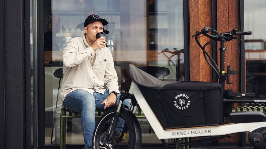 Mann drikker kaffe på cafe ved siden av elektrisk lastesykkel