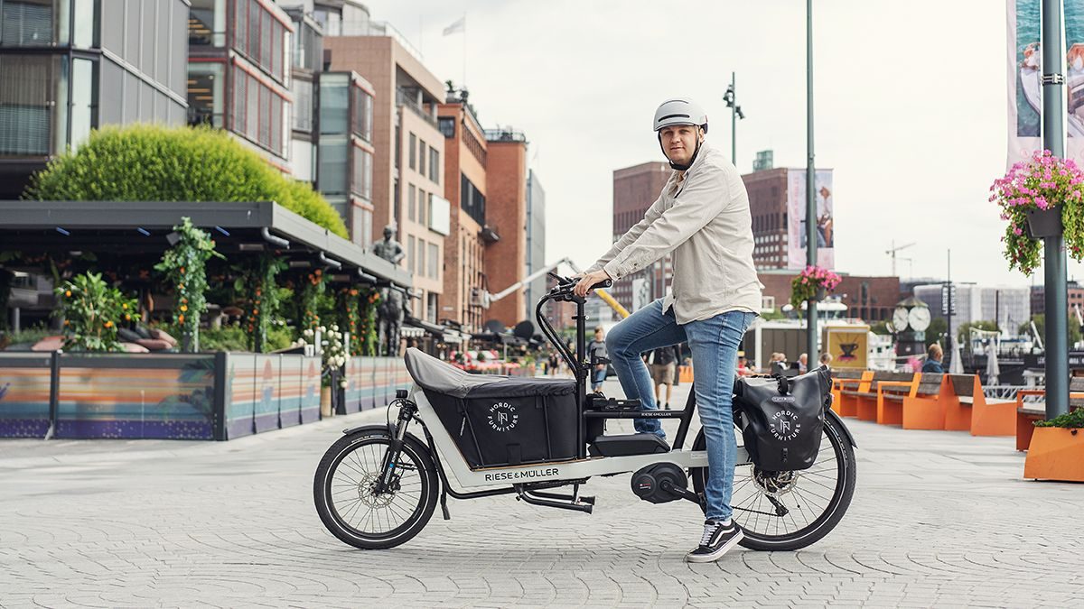 En mann som kjører en elektrisk lastesykler med en kurv på.