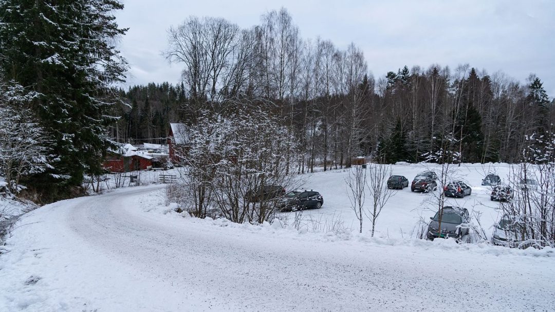 Snødekket vei og parkeringsplass med sportsstue i bakgrunnen.