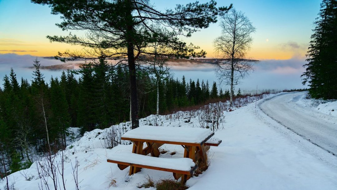 Benk på snødekketvei med utsikt i bakgrunnen.