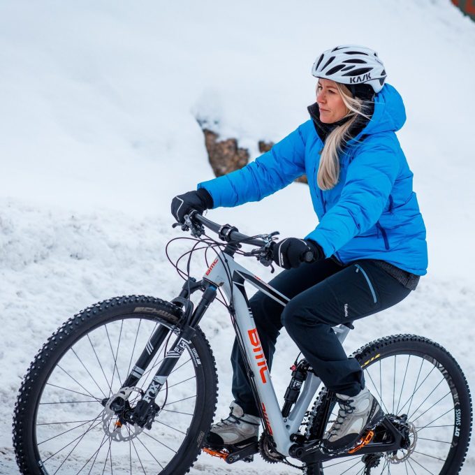 En person i blå jakke og hjelm nyter litt vintersykling, og navigerer dyktig med terrengsykkelen sin langs en snødekt sti.