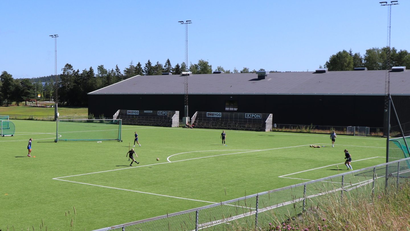 fotballspillere trener på kunstgressbane i sollys og blå himmel
