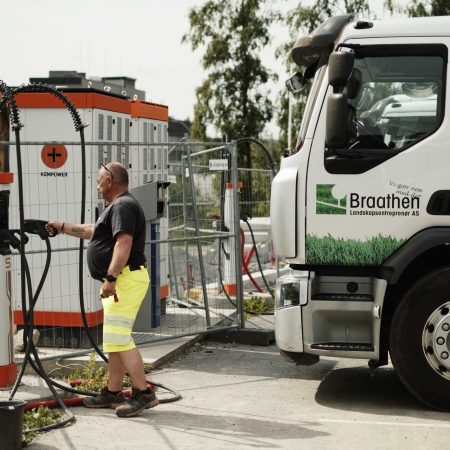 En lastebilsjåfør i arbeidsklær setter en ladeplugg tilbake i hurtigladeren utenfor fronten på lastebilen