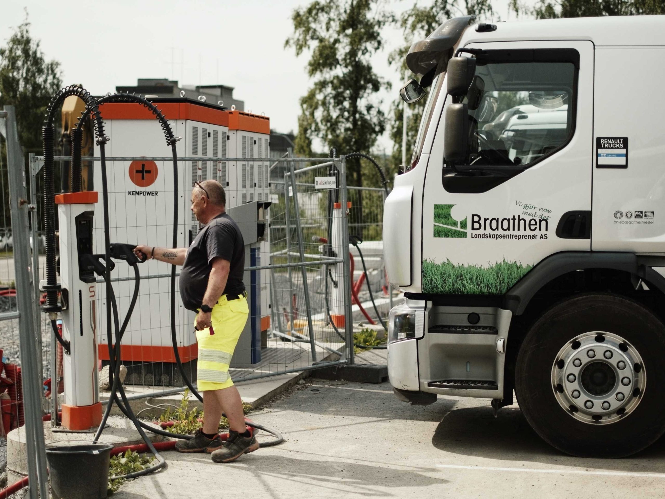 En lastebilsjåfør i arbeidsklær setter en ladeplugg tilbake i hurtigladeren utenfor fronten på lastebilen