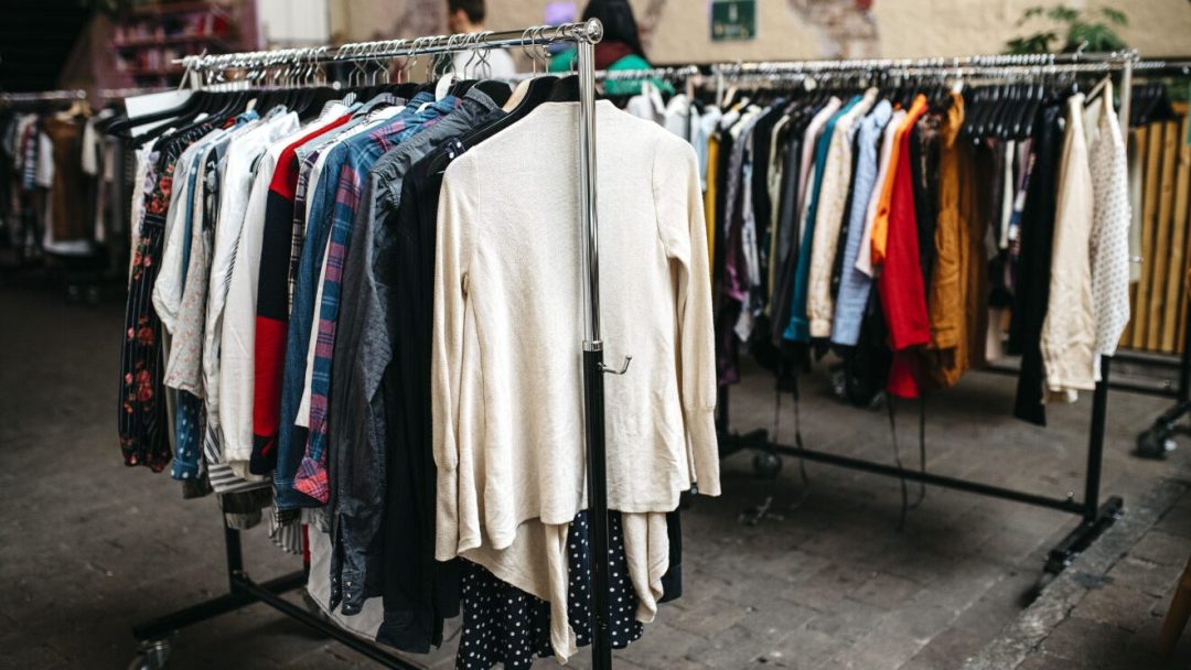 Klesstativer med ulike plagg, som fremmer en mindre for klima livsstil, vises utendørs på en asfaltert overflate.