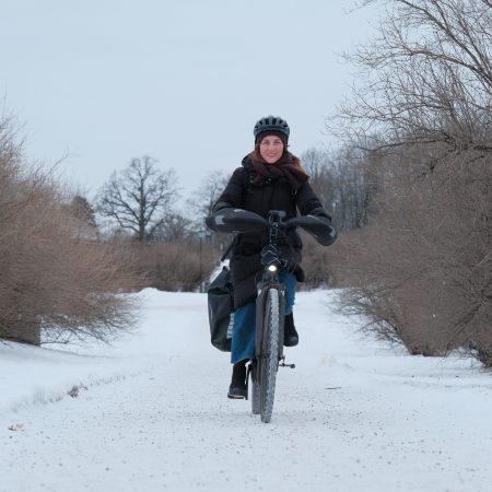 En person med hjelm og vinterklær sykler på en snødekt sti med nakne trær.