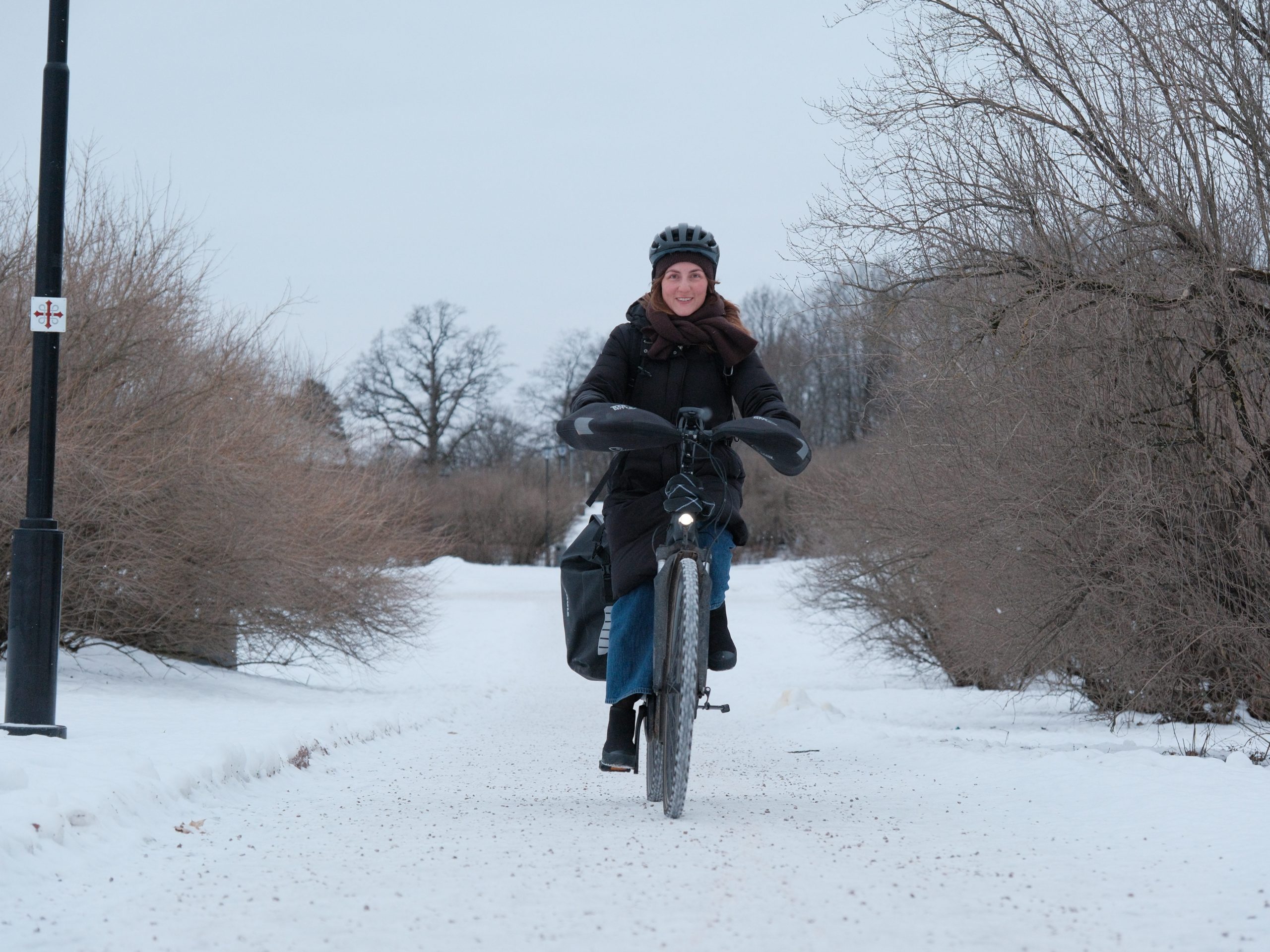 En person med hjelm og vinterklær sykler på en snødekt sti med nakne trær.