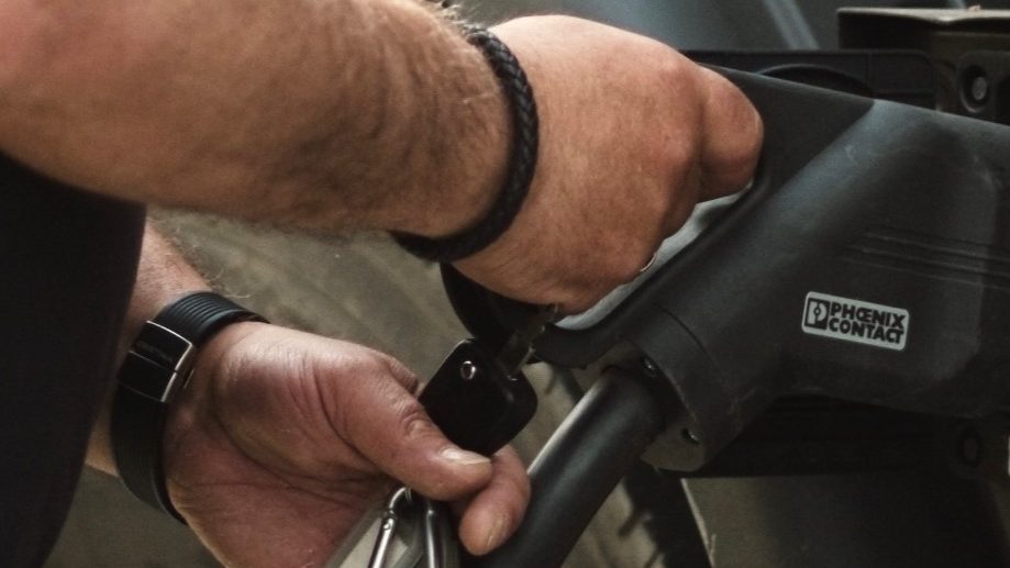 En person er på jobben, fyller drivstoff på et kjøretøy, holder en drivstoffdyse i den ene hånden og en nøkkelring i den andre, nær et stort hjul.